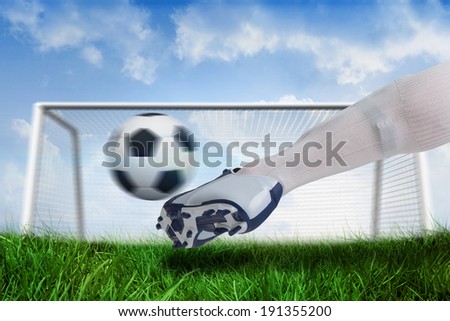 Composite image of close up of football player kicking ball against goalpost on grass under blue sky