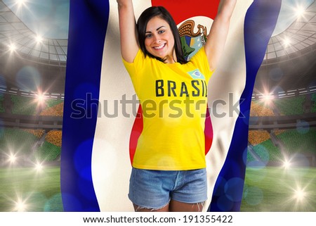 Excited football fan in brasil tshirt holding costa rica flag against large football stadium with brasilian fans