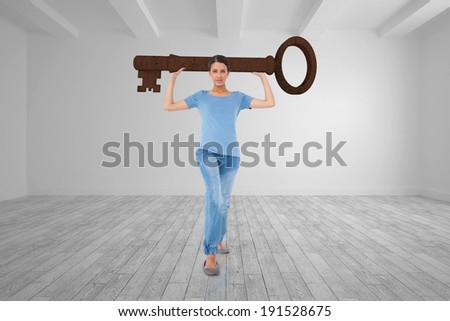 Annoyed brunette carrying large key against big room with white wall