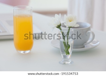 White flower in a vase with coffee and orange juice on table at home in the living room