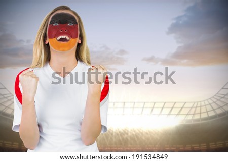 Excited german fan in face paint cheering against large football stadium under cloudy blue sky