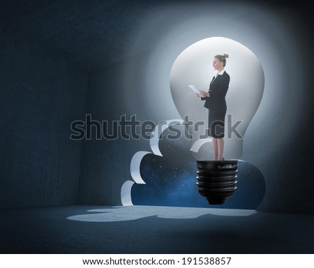 Businesswoman holding tablet in light bulb against cloud door in dark room