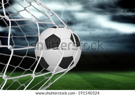 Football at back of net against football pitch under stormy sky