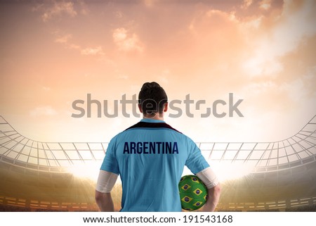 Argentina football player holding ball against large football stadium under cloudy blue sky