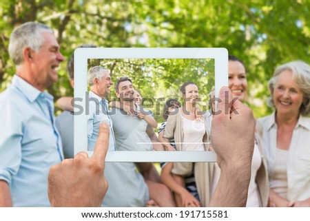 Hand holding tablet pc showing extended family spending time in the park