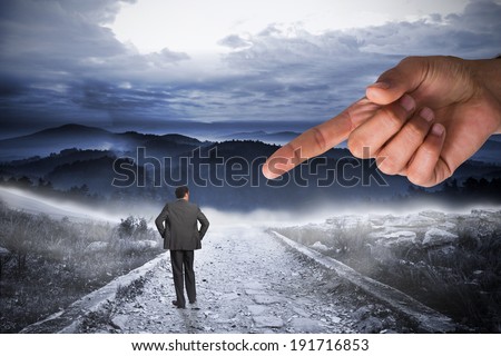 Giant hand pointing at businessman with hands on hips against stony path leading to large misty mountains