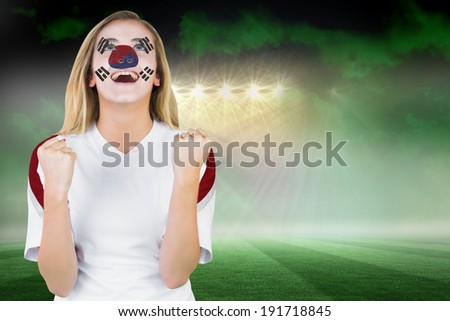 Excited south korea fan in face paint cheering against football pitch under green sky and spotlights