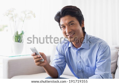 Happy man sitting on couch texting on phone at home in the living room