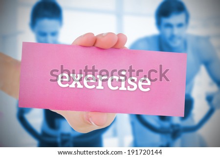 Woman holding pink card saying exercise against fitness class in gym