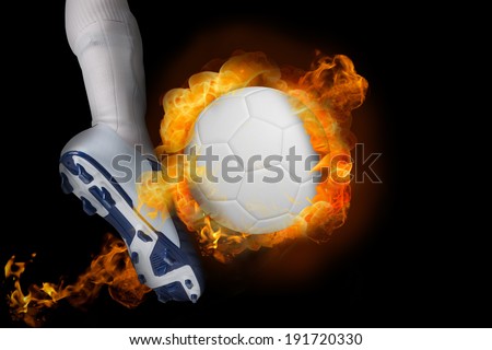 Football player kicking flaming ball against black