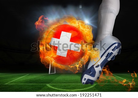 Football player kicking flaming swiss flag ball against football pitch and goal under spotlights