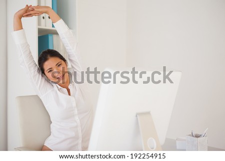 Casual businesswoman stretching at her desk in her office
