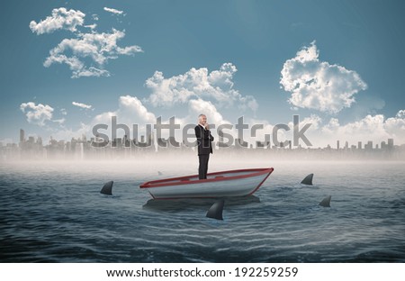 Happy businessman looking away against sharks circling a small boat in the sea