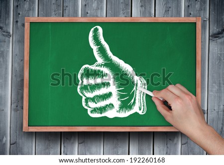 Composite image of hand drawing thumbs up with chalk on chalkboard on grey wooden planks