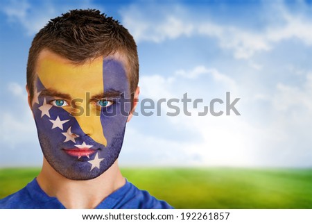 Composite image of bosnia football fan in face paint against football pitch under blue sky