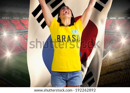 Excited football fan in brasil tshirt against holding south korea flag vast football stadium with fans in yellow and red