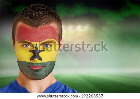 Composite image of ghana football fan in face paint against football pitch under green sky and spotlights