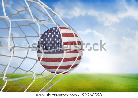 Football in america colours at back of net against football pitch under blue sky
