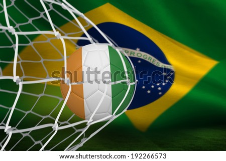 Football in ivory Coast colours at back of net against brazilian flag waving