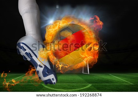 Football player kicking flaming germany flag ball against football pitch and goal under spotlights