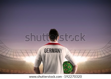 Germany football player holding ball against large football stadium under blue sky