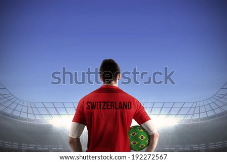 Swiss football player holding ball against large football stadium under bright blue sky