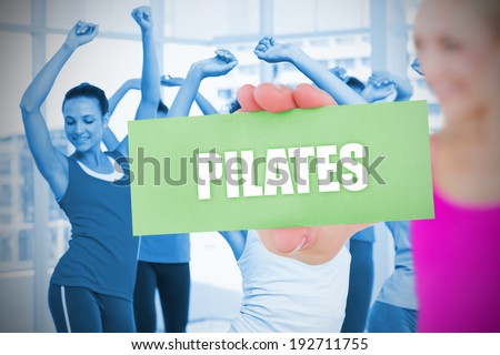 Fit blonde holding card saying pilates against fitness class in gym