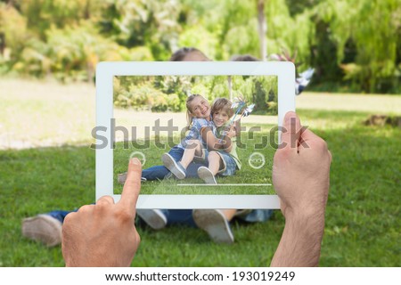 Hand holding tablet pc showing cute siblings sitting in the park