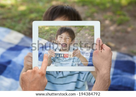 Hand holding tablet pc showing happy boy holding block alphabets as play at park