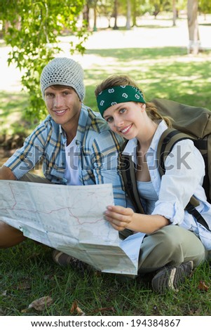 Active smiling couple sitting down on a hike holding map on a sunny day