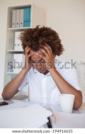 Casual stressed businessman with his head down at desk in his office