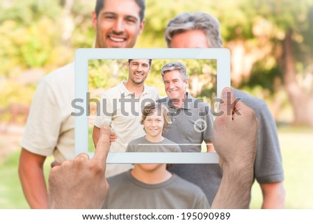 Hand holding tablet pc showing family looking at the camera in the park