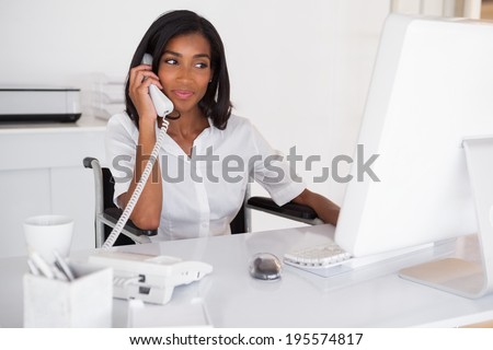 Happy businesswoman in wheelchair working at her desk in her office