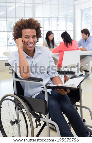 Businessman in wheelchair holding planner and smiling at camera in the office