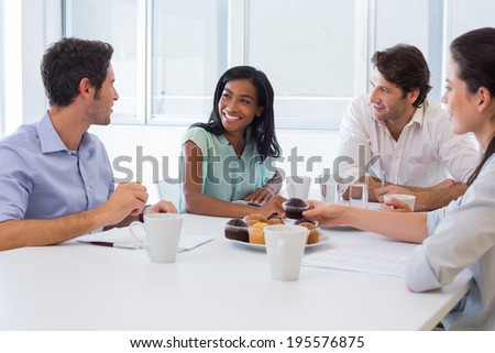 Work colleagues chatting in board room while enjoying coffee and muffins in the office