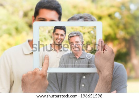 Hand holding tablet pc showing father with his son looking at the camera