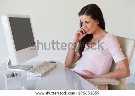 Casual pregnant businesswoman thinking at her desk in her office