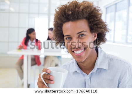 Businessman relaxing with coworkers behind him in the office