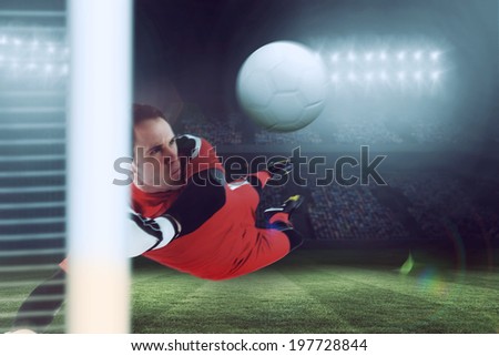 Fit goal keeper jumping up against large football stadium under blue sky