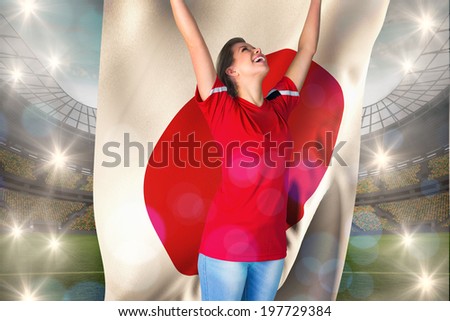 Cheering football fan in red holding japan flag against large football stadium with lights