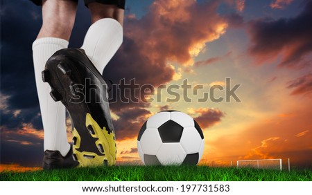 Composite image of football boot kicking ball against green grass under dark blue and orange sky