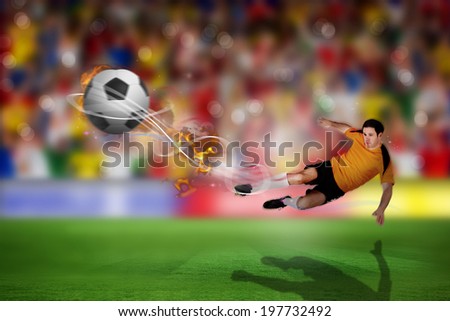 Football player in orange kicking against blurry football pitch with crowd