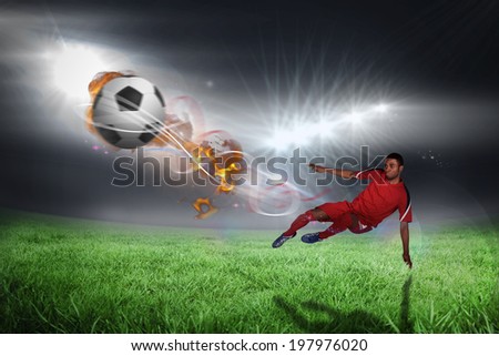 Football player in red kicking against football pitch under bright lights