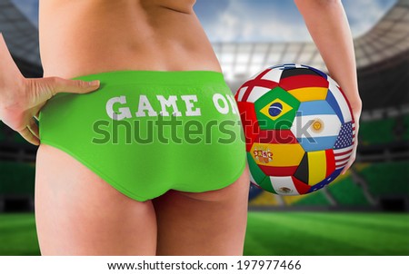 Fit girl in green bikini holding flag football against large football stadium with brasilian fans