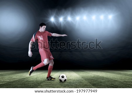 Football player in red kicking against football pitch under spotlights