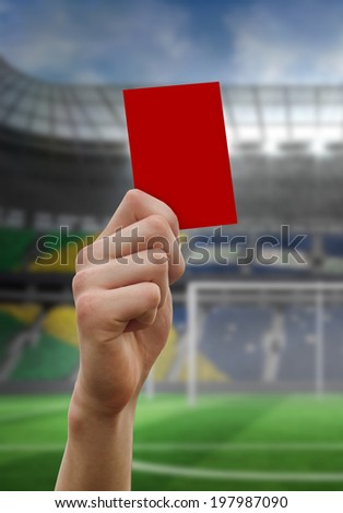 Hand holding up red card against football pitch in large stadium
