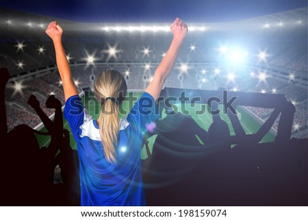 Cheering football fan in blue against large football stadium with lights