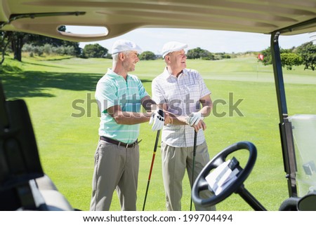 Golfing friends standing beside their buggy looking around on a sunny day at the golf course