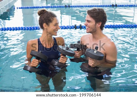 Man and woman standing with foam dumbbells in the pool at the leisure center