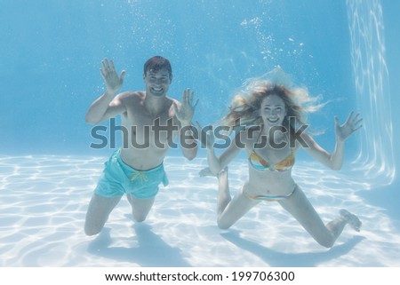 Cute couple smiling at camera underwater in the swimming pool on their holidays